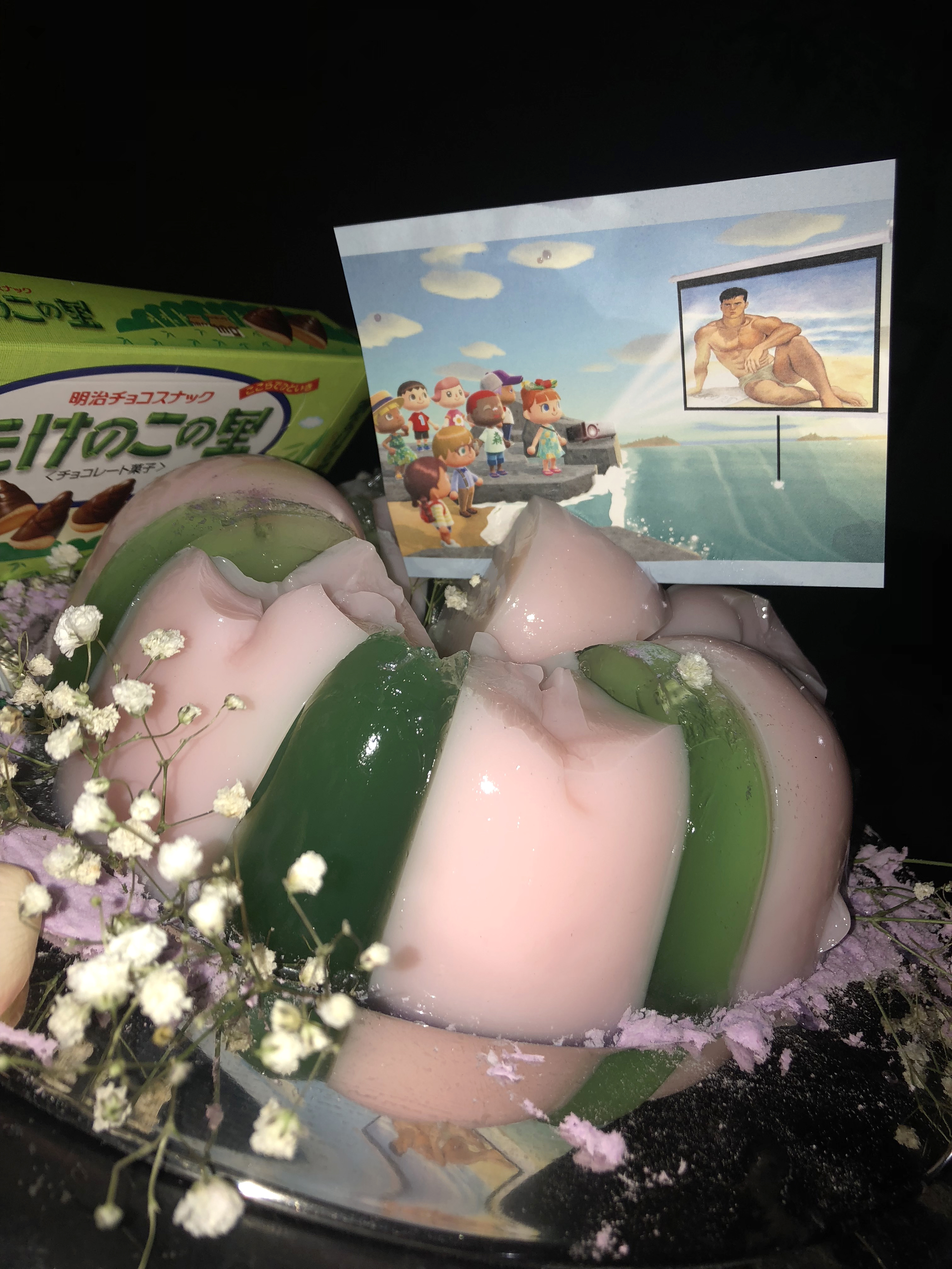 A postcard shoved in a pink and green jello cake which has been partially eaten